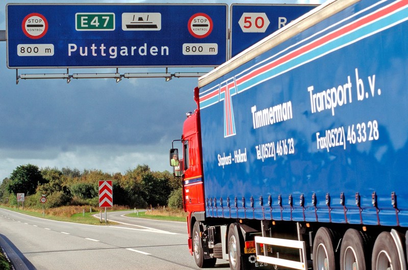 En blå lastbil kører under et motorvejsskilt hvorpå der står Puttgarden.