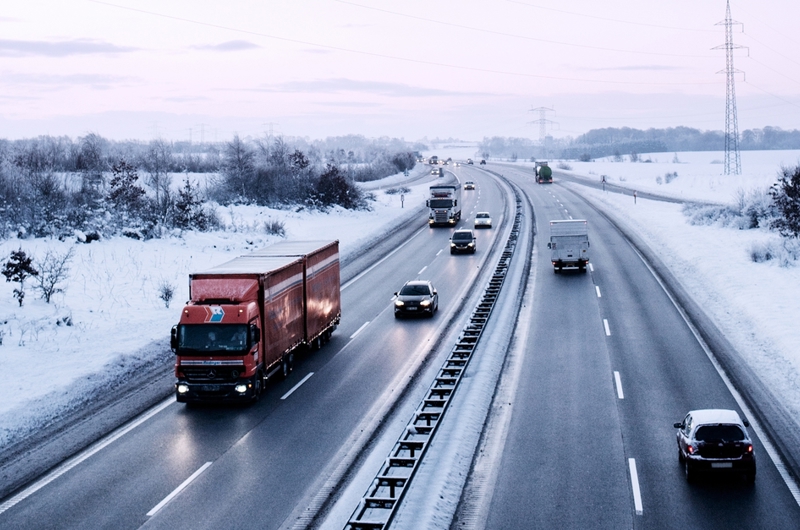 Biler og lastbiler kører på en sneryddet motorvej, imens sneen ligger på markerne ved siden af.