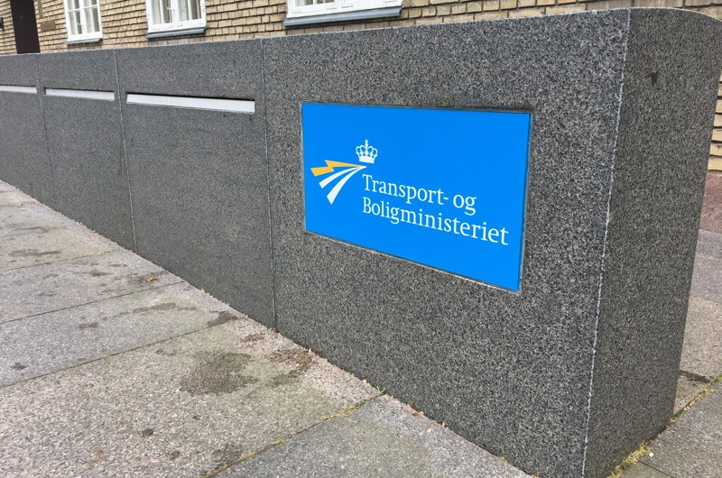 Et skilt med transport- og boligministeriets logo sidder i en mur af granit.