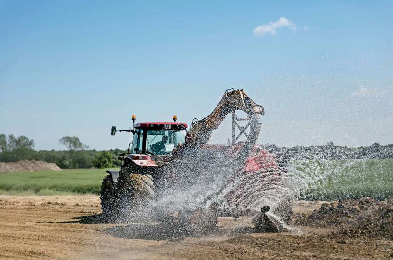 Foto af rød traktor, der kører på en mark med et påhængskøretøj bagefter, imens den udfører markarbejde.